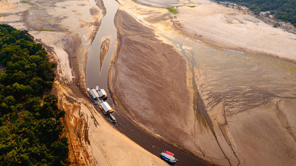 Imagem área de um rio seco, com pouca vegetação nas laterais e um rio muito estreito rodeado de terra. Há poucos barcos neste rio. 
